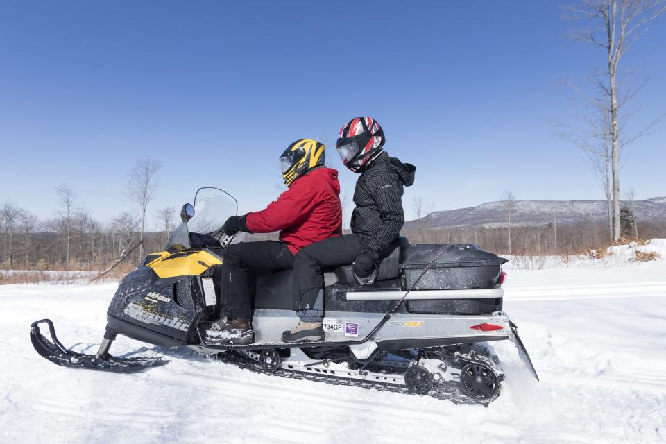 Two snowmobilers ride on a snowmobile on a sunny day.