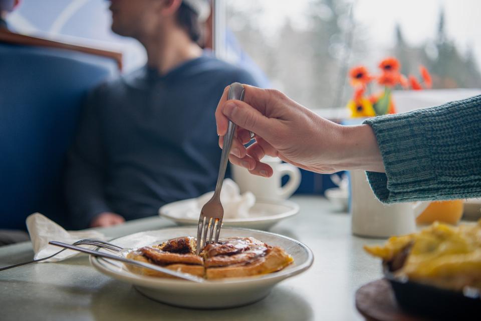 A close up of someone digging their fork into a cinnamon bun at a diner.