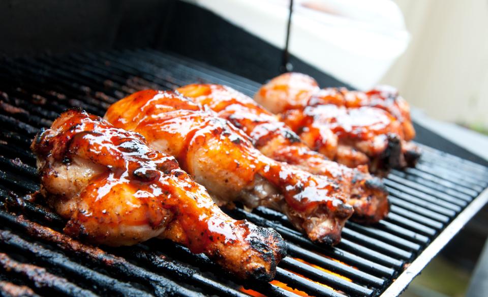 Several pieces of chicken covered in bbq sauce grilling on a black grill rack