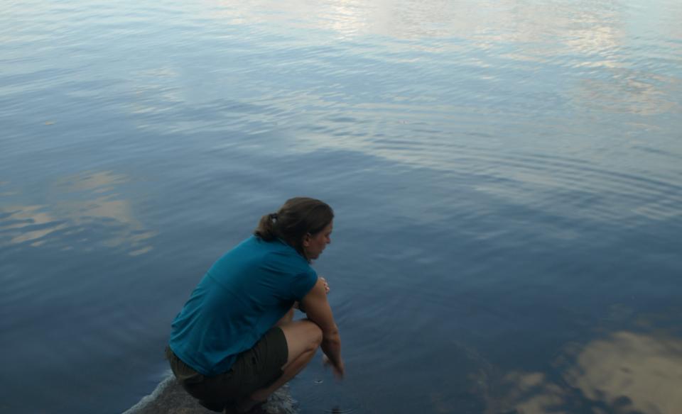 A person kneels down by the water.