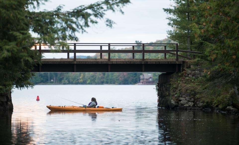 A kayaker fishing underneath a wooden bridge.