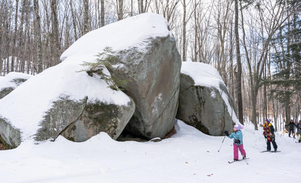 Two kids cross-country ski past tall boulders