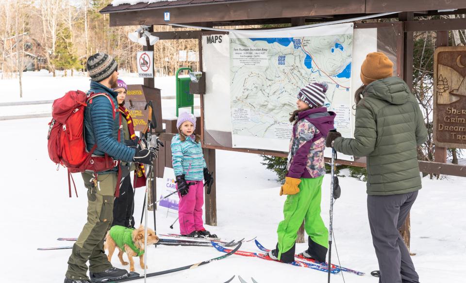 A family at a trailhead kiosk about to cross-country ski