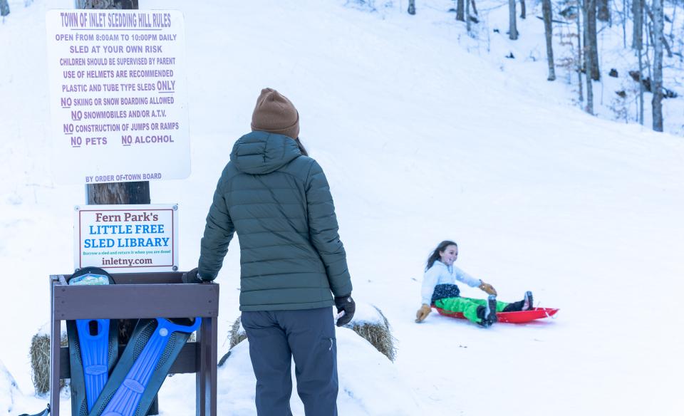 A kid sledding down a hill as her parent watches.