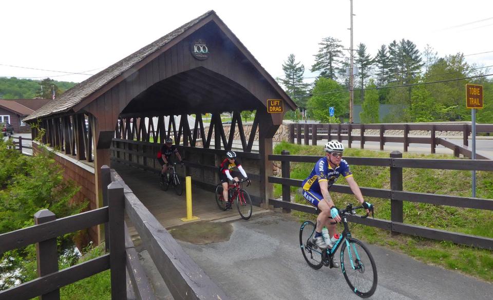 People bike over a small covered bridge